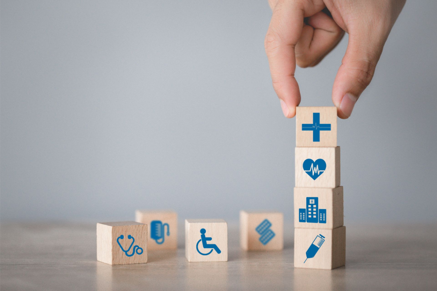 Hand placing a medical cross block onto a stack of healthcare icons on wooden cubes
