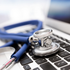 Stethoscope on laptop keyboard with pen and blue notebook, suggesting telehealth or online medical work