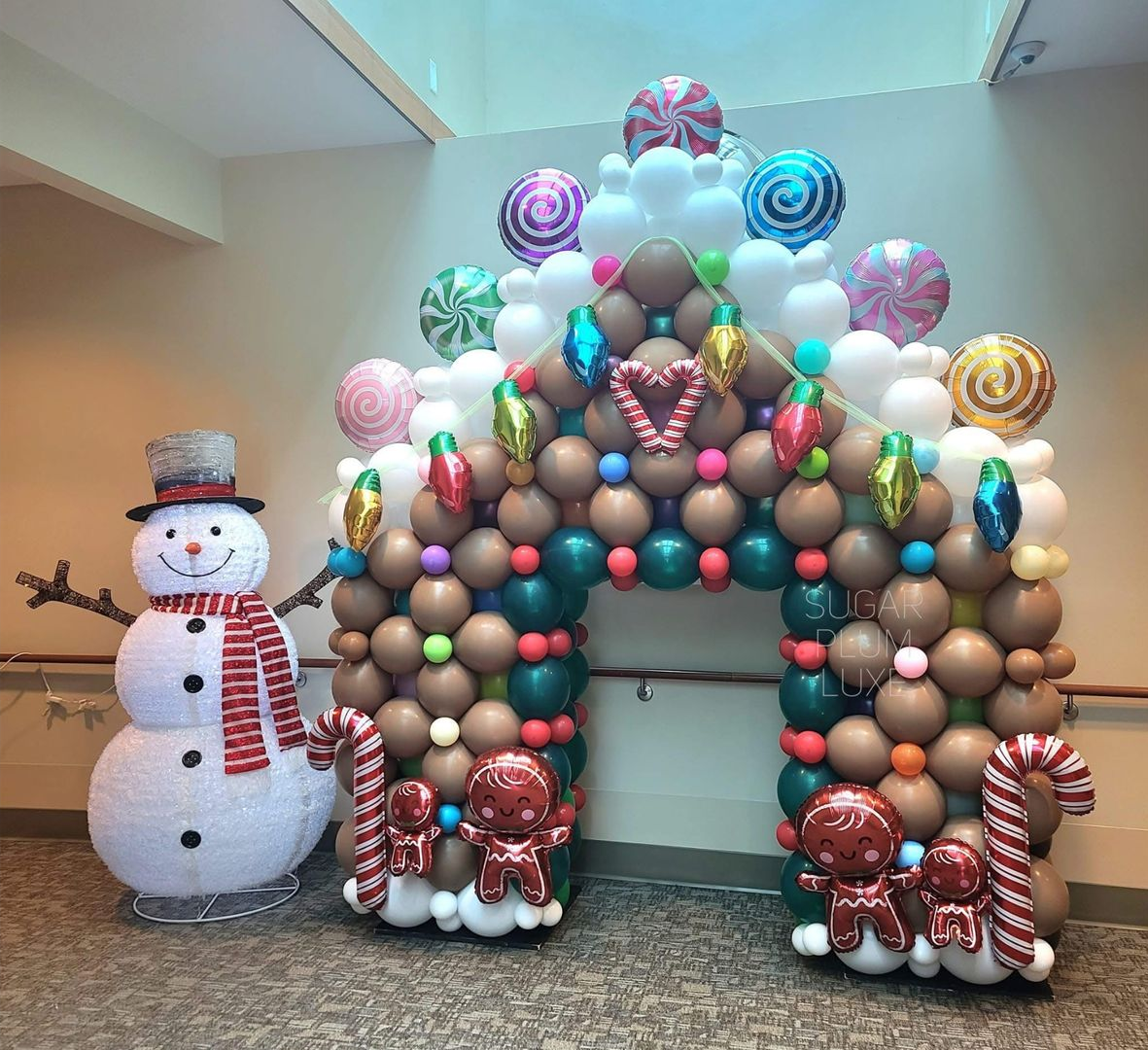 Snowman and balloon arch holiday display with red-and-white candy cane accents indoors