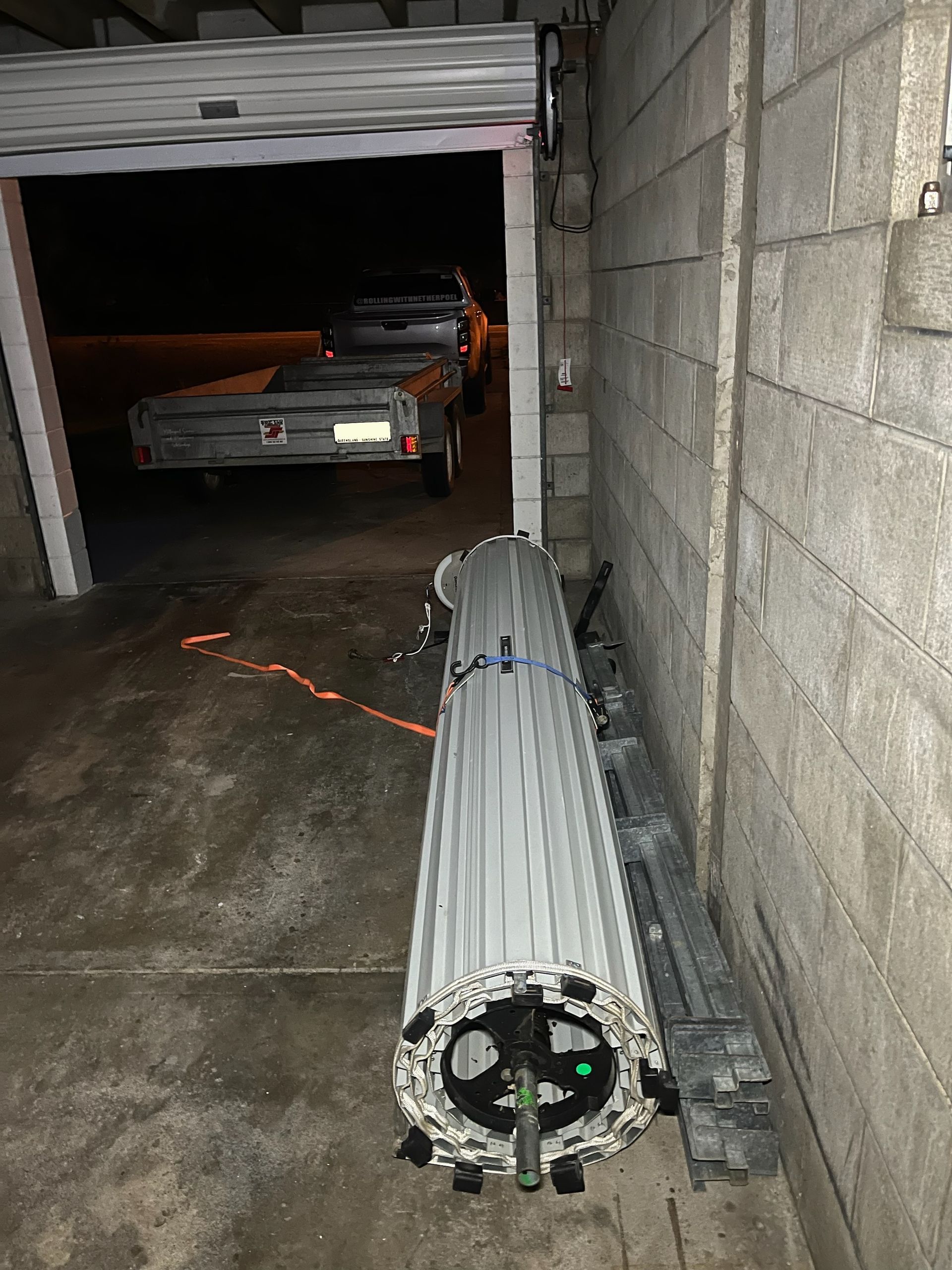 Rolled-up silver metal duct in a dim garage, with a car parked inside — Rolling With Netherpoel in Bowen, QLD