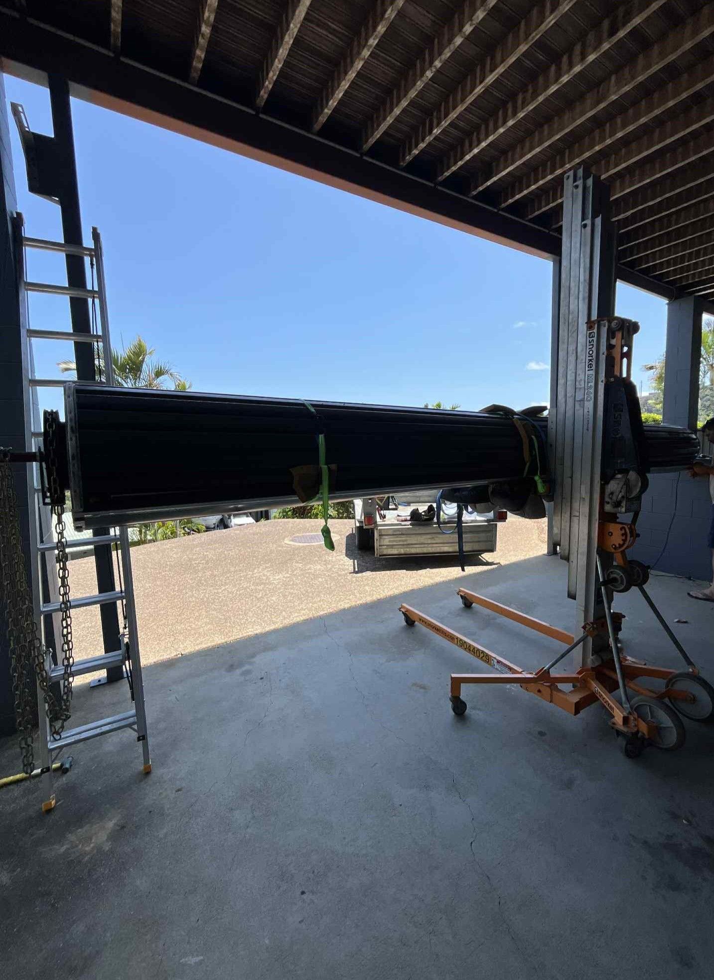 Large black pipe being lifted in a warehouse doorway with a ladder and machinery nearby — Rolling With Netherpoel in Bowen, QLD