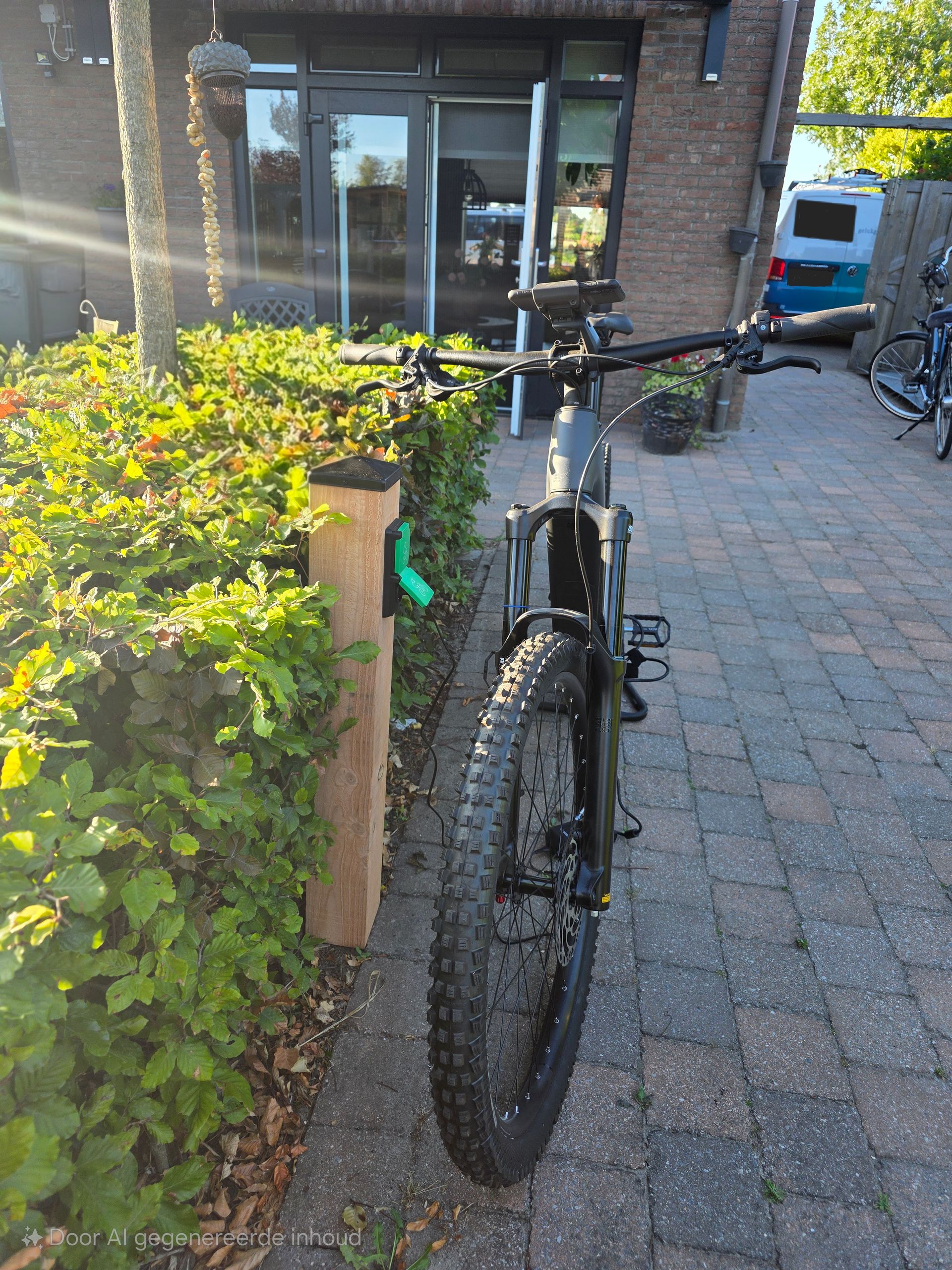 Een zwarte fatbike staat geparkeerd naast groene struiken op een stenen pad voor een huis.