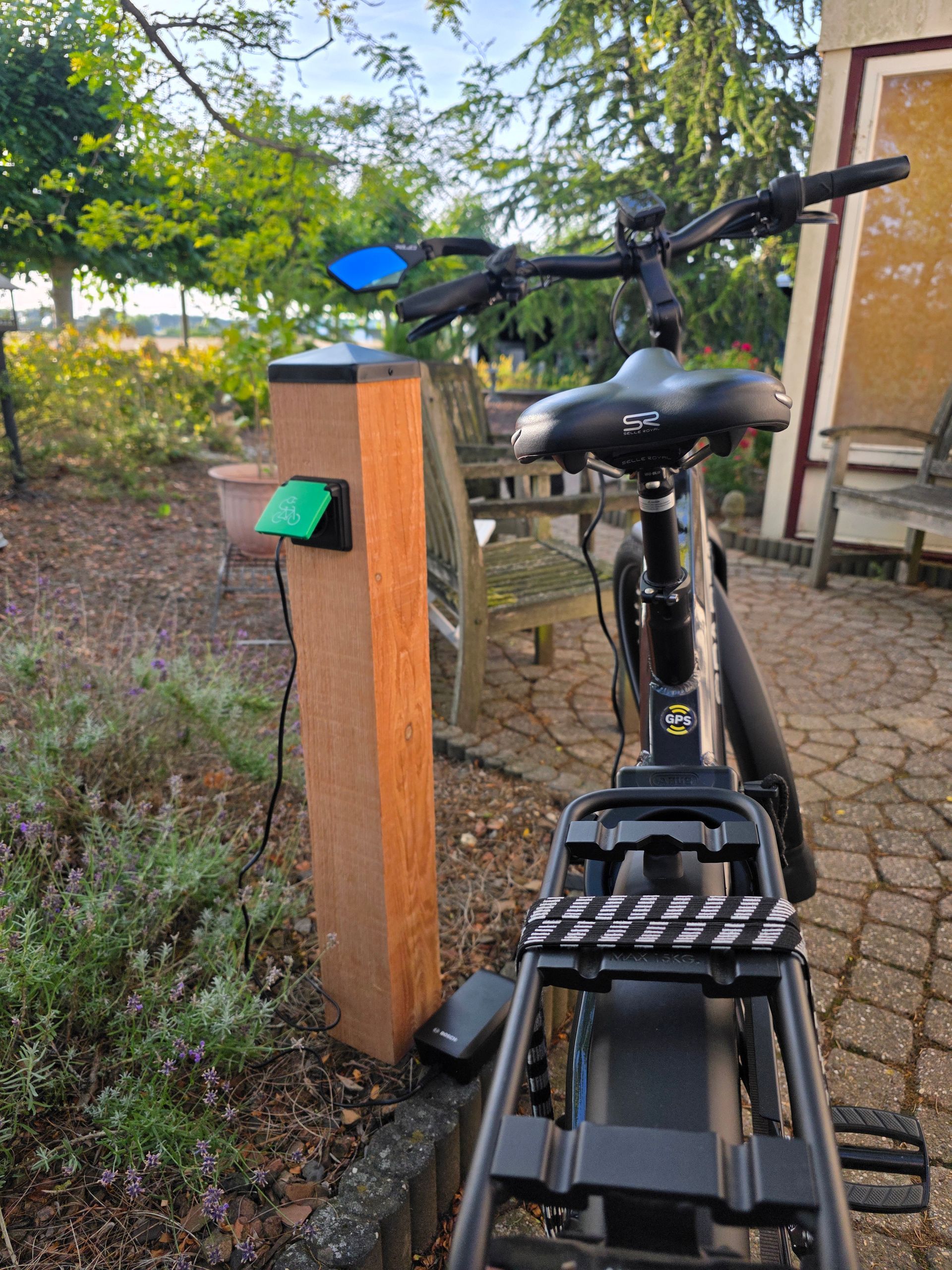 Elektrische fietsen worden opgeladen bij een houten paal met een groen stopcontact in een buitenomgeving.
