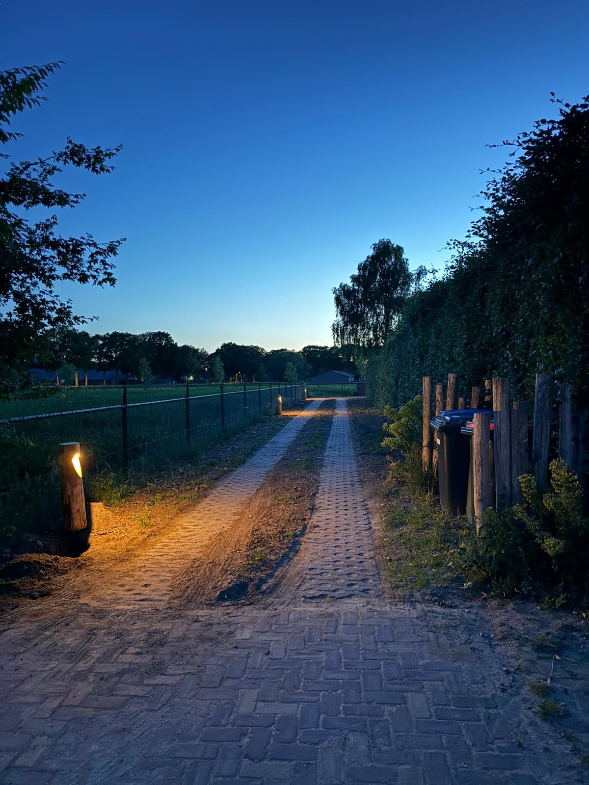 Een grindpad, verlicht door lampen, leidt door een groene ruimte onder een donkerblauwe hemel.