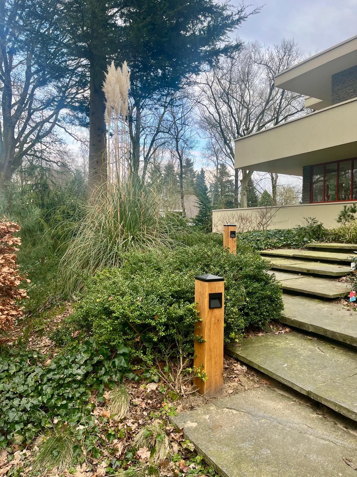 Houten paal met een zwarte vierkante lamp in een tuin.
