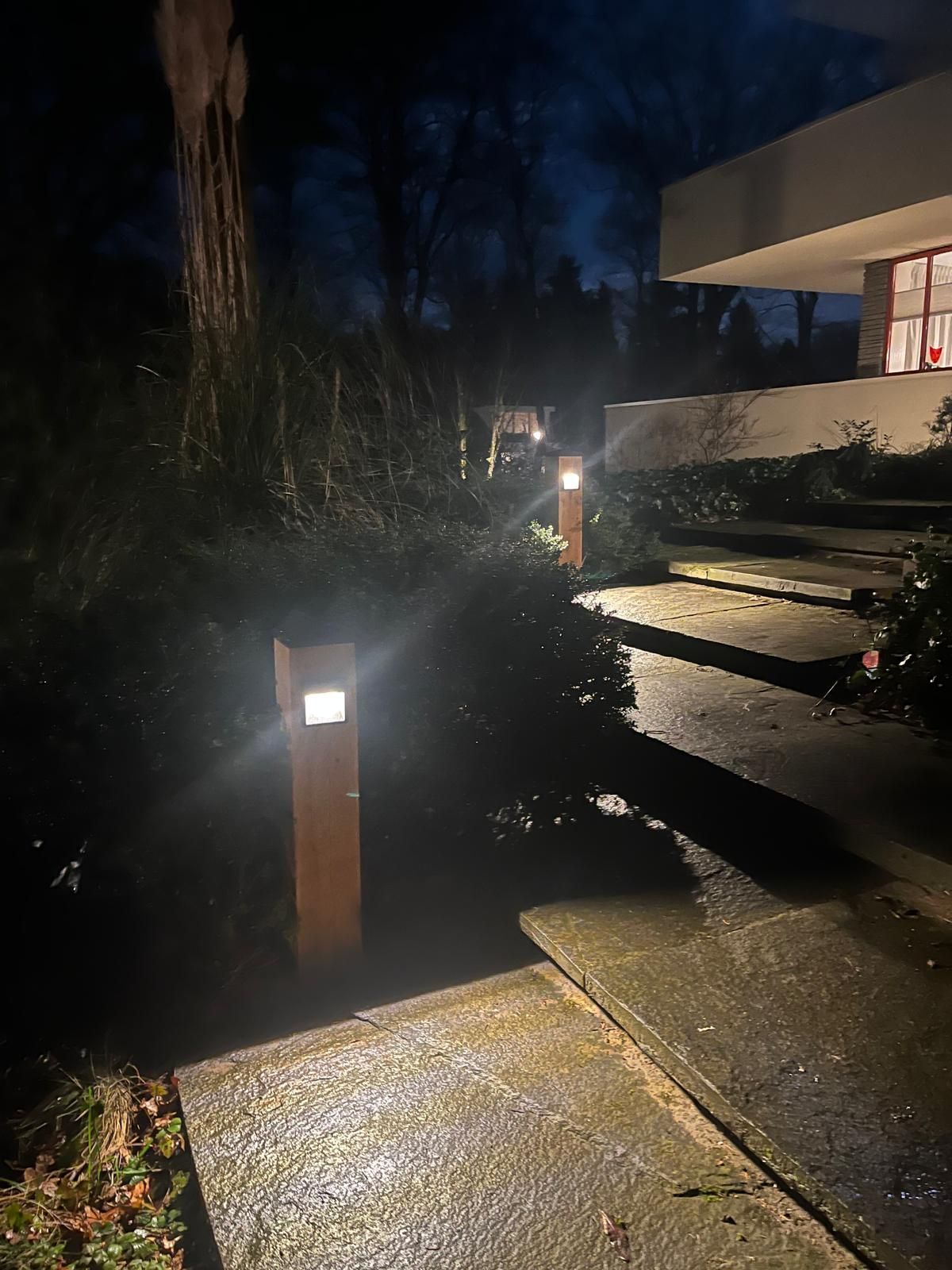 Nachtelijk uitzicht op een voetpad, verlicht door paaltjes, dat leidt naar een huis met verlichte ramen.