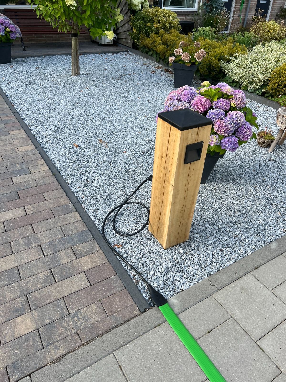 Houten paal met zwarte bovenkant en uitlaat op een grindbed met hortensia's.
