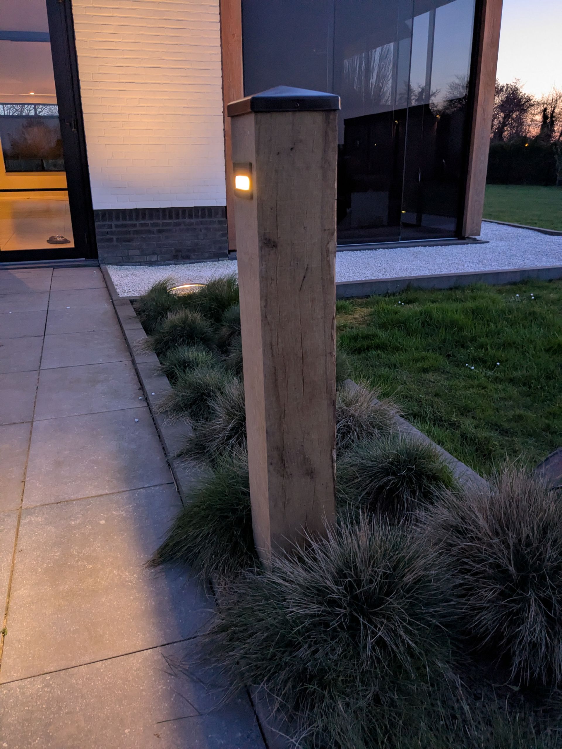 Houten paal met geïntegreerde verlichting naast een bestraat pad en een grasveld.