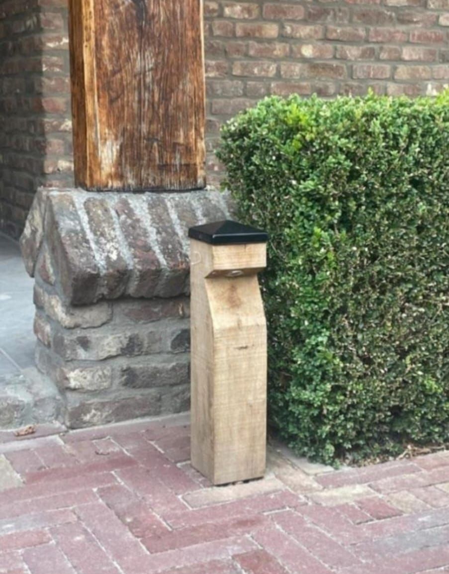 Houten paaltje met zwarte bovenkant naast een groene heg en een bakstenen pad.