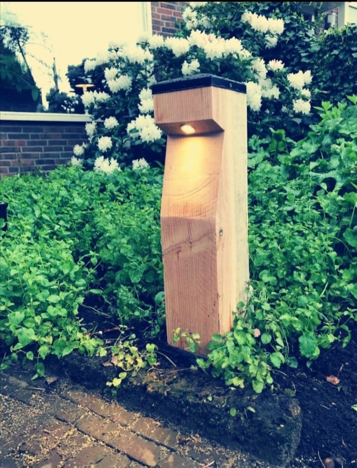Houten paaltje met zwarte bovenkant naast een groene heg en een bakstenen pad.
