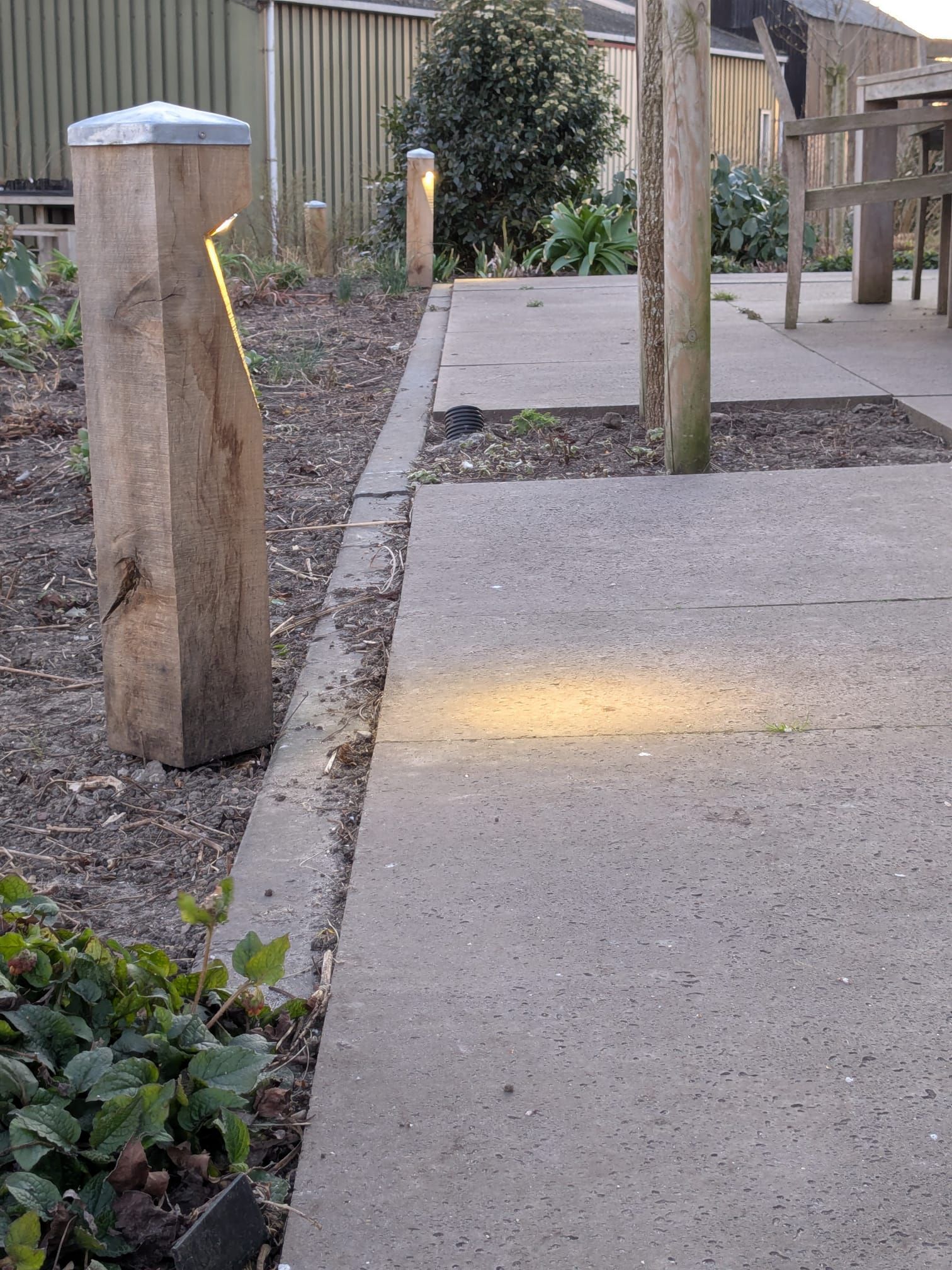 Houten paal met een gloeiend amberkleurig licht, voor een waterput op een grasheuvel, in de schemering.