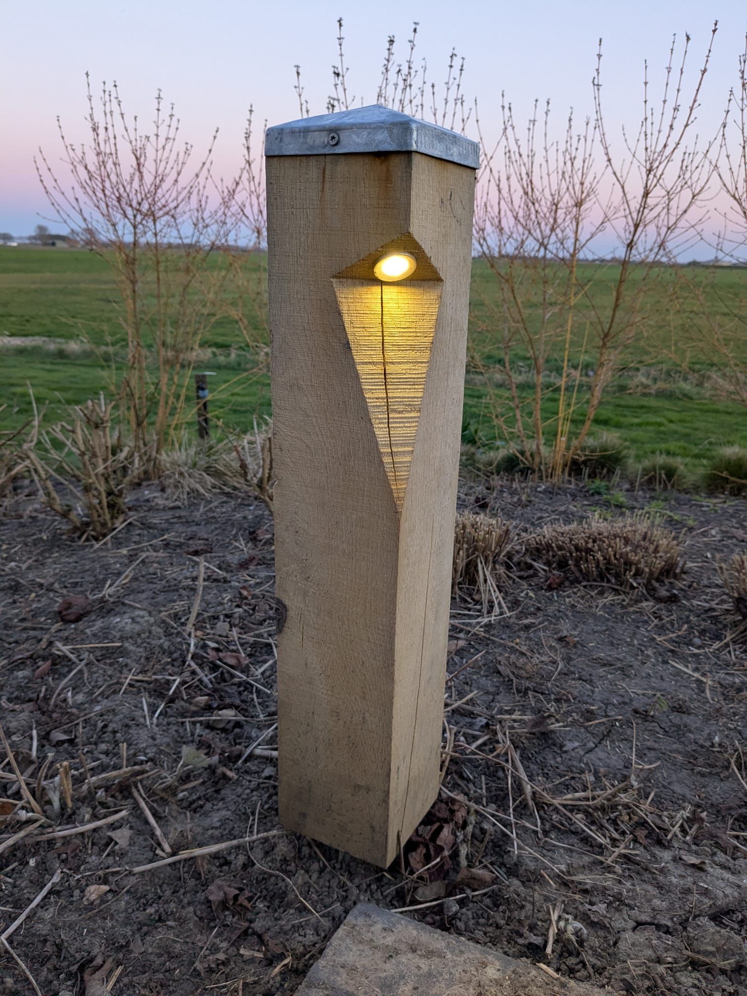 Stenen padverlichting met een ruitvormige uitsparing die een warme gloed verspreidt; geschikt voor de schemering.