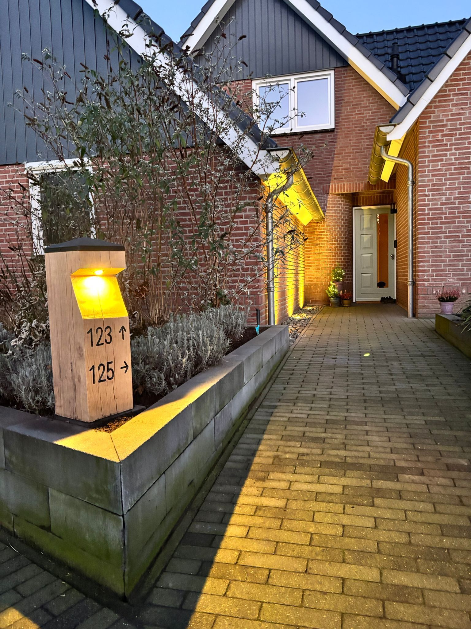 De buitenkant van een bakstenen huis met een verlichte adrespaal en een voetpad.