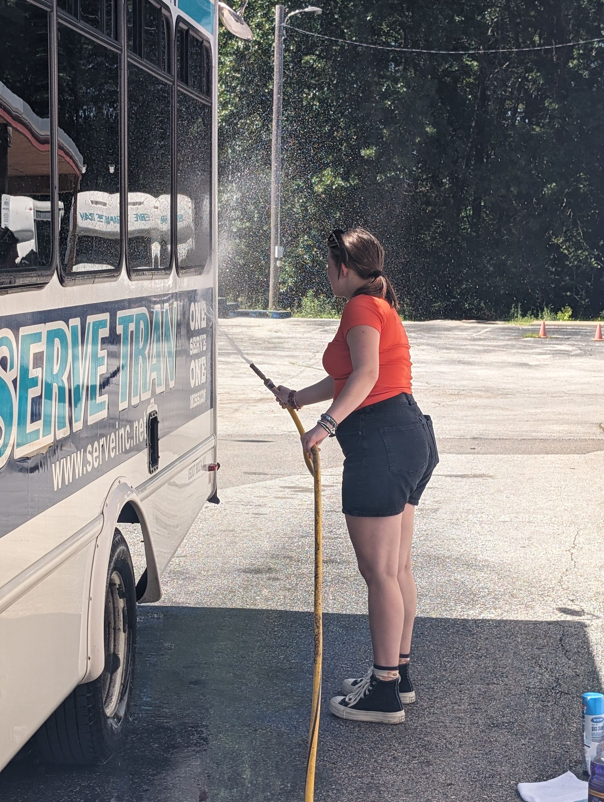 A woman is washing a bus with a hose.