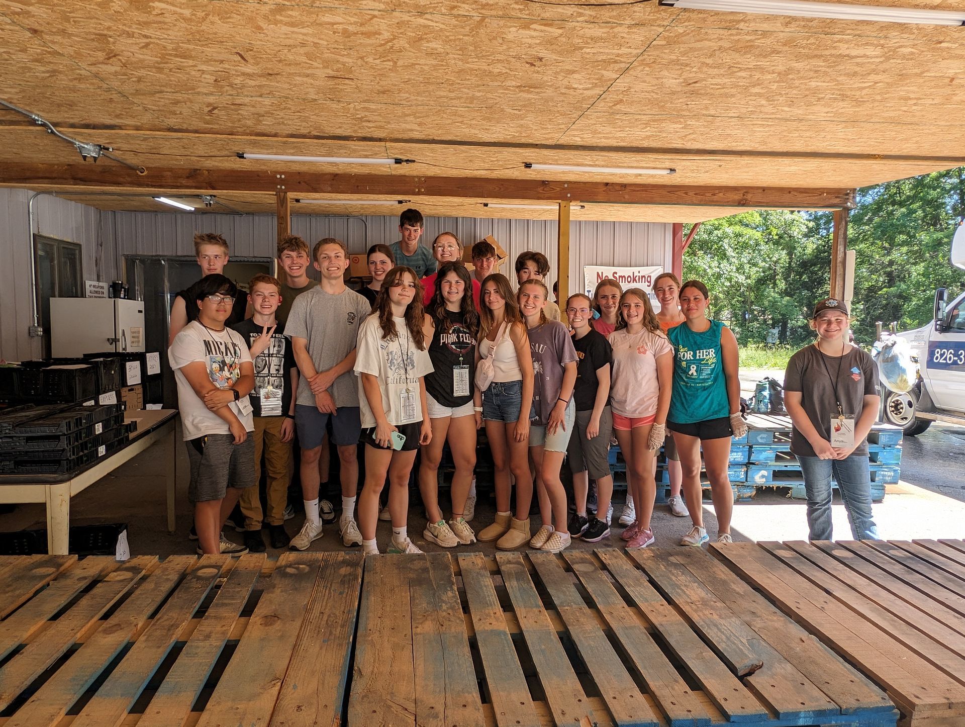 A group of young people are posing for a picture in front of a wooden pallet.
