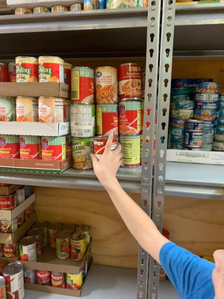 A person is reaching for a can of soup in a pantry.