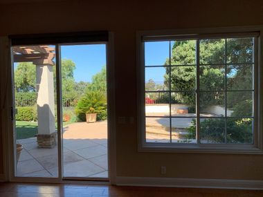 Empty room with sliding glass door and window opening to a sunny patio and garden