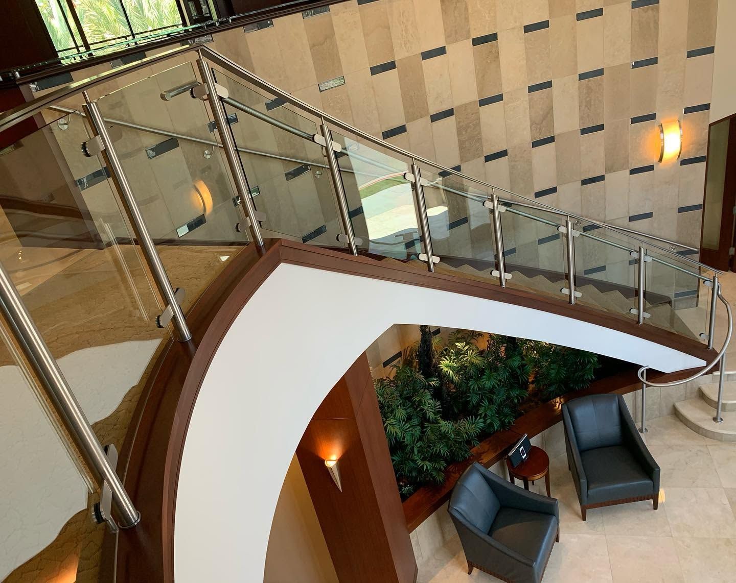 Modern indoor atrium with curved staircase, glass railing, and lounge chairs below