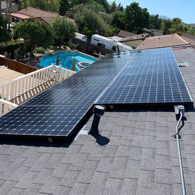 Solar panels on a rooftop overlooking a backyard pool and suburban homes.