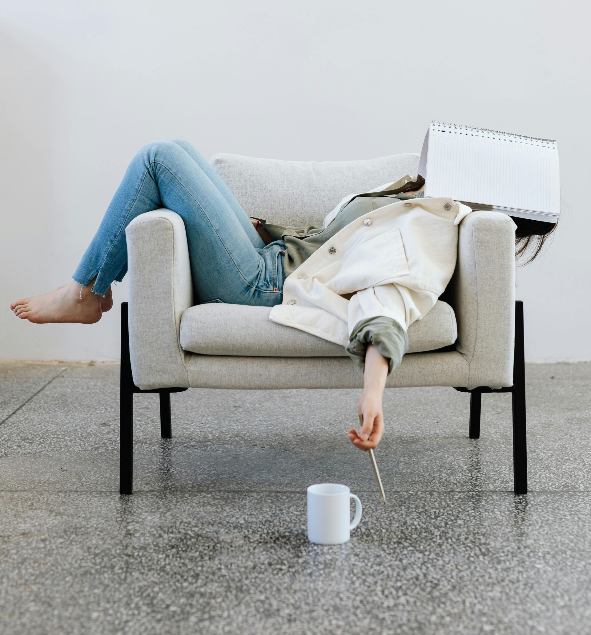Person slumped in a chair, a white mug and hand holding a stick near the floor, head obscured by a device.