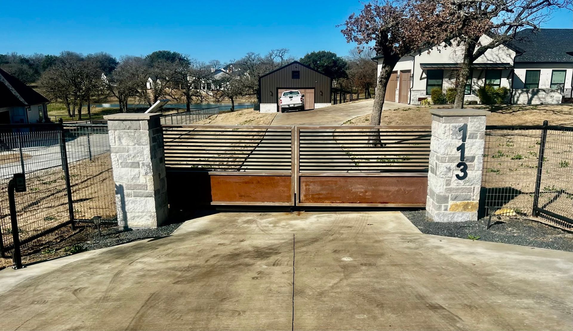 Closed gate at a rural driveway with stone pillars and a house in the background
