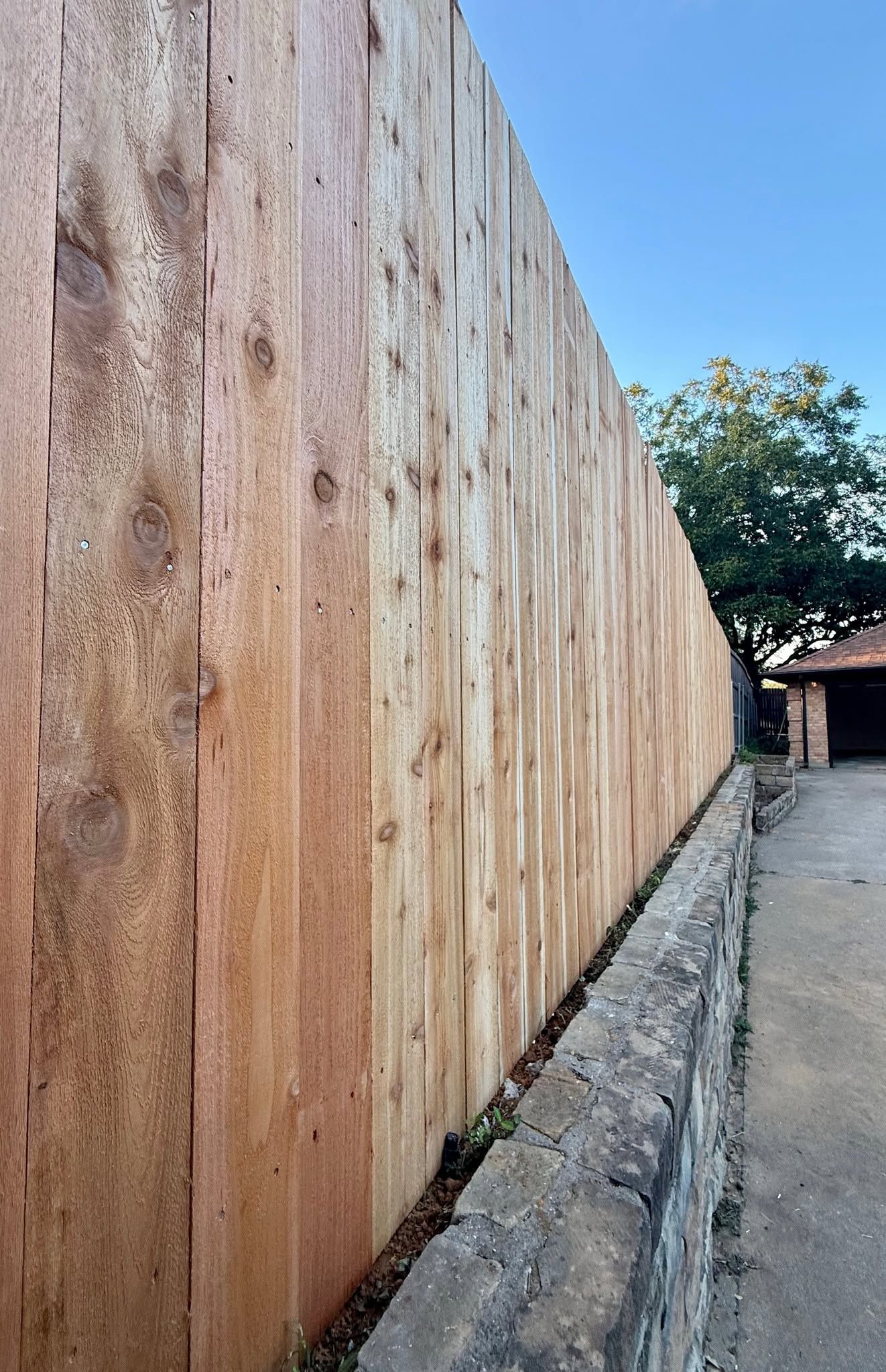 Tall rust-stained wall beside a narrow paved alley under a blue sky