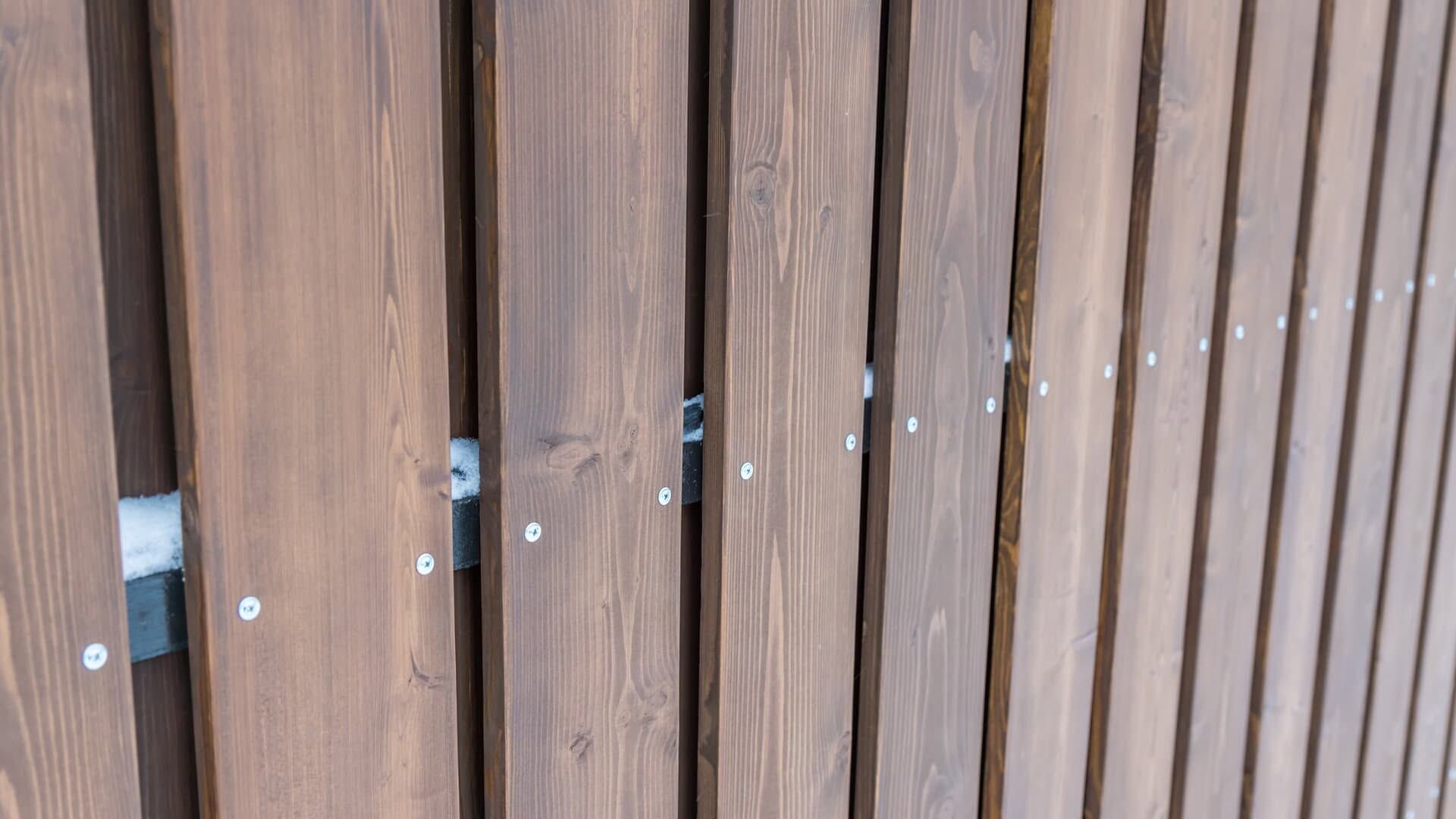 Close-up of a weathered wooden fence with vertical brown slats and visible metal bolts