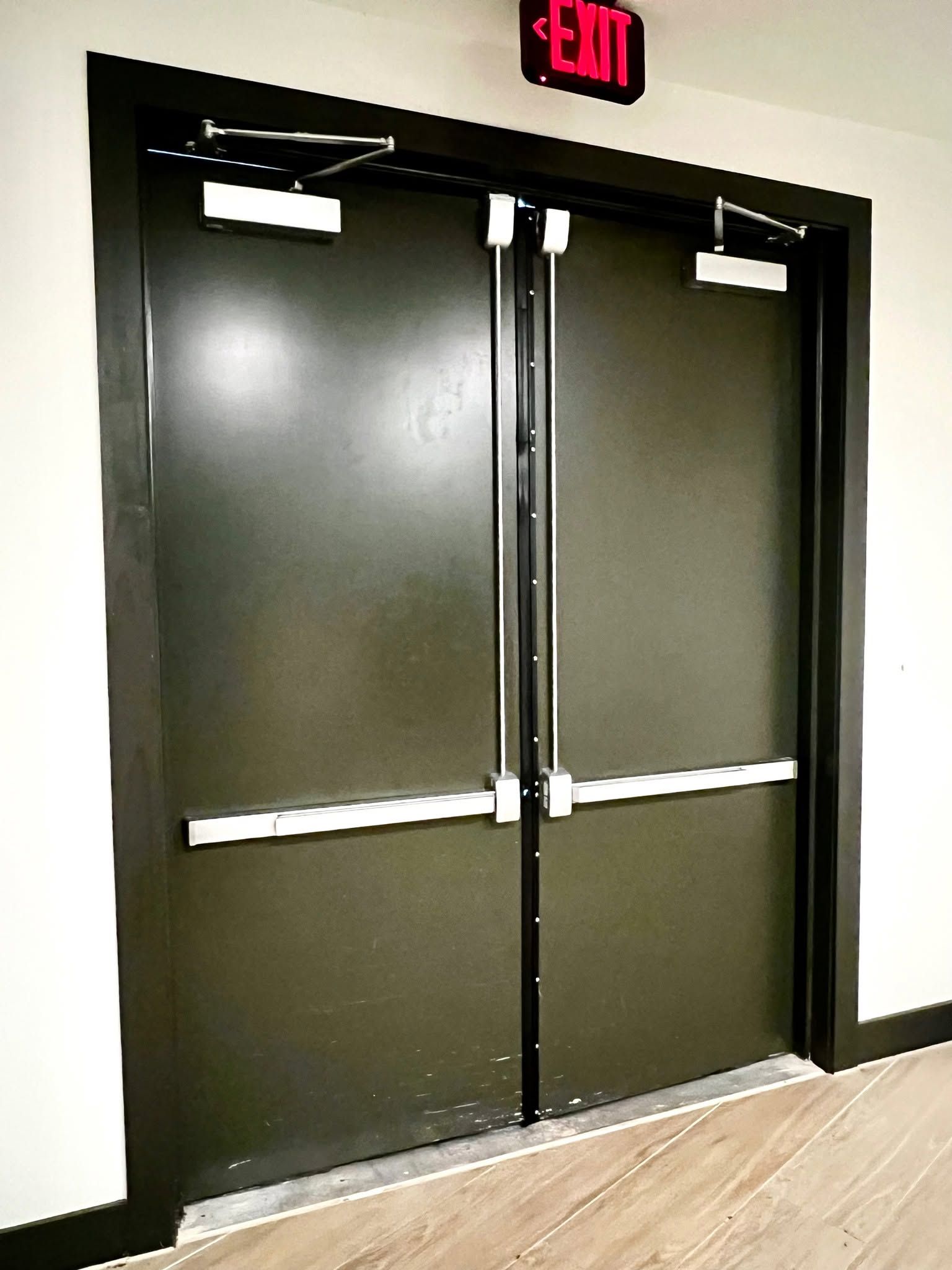 Closed dark double doors with a red exit sign above them in a hallway.