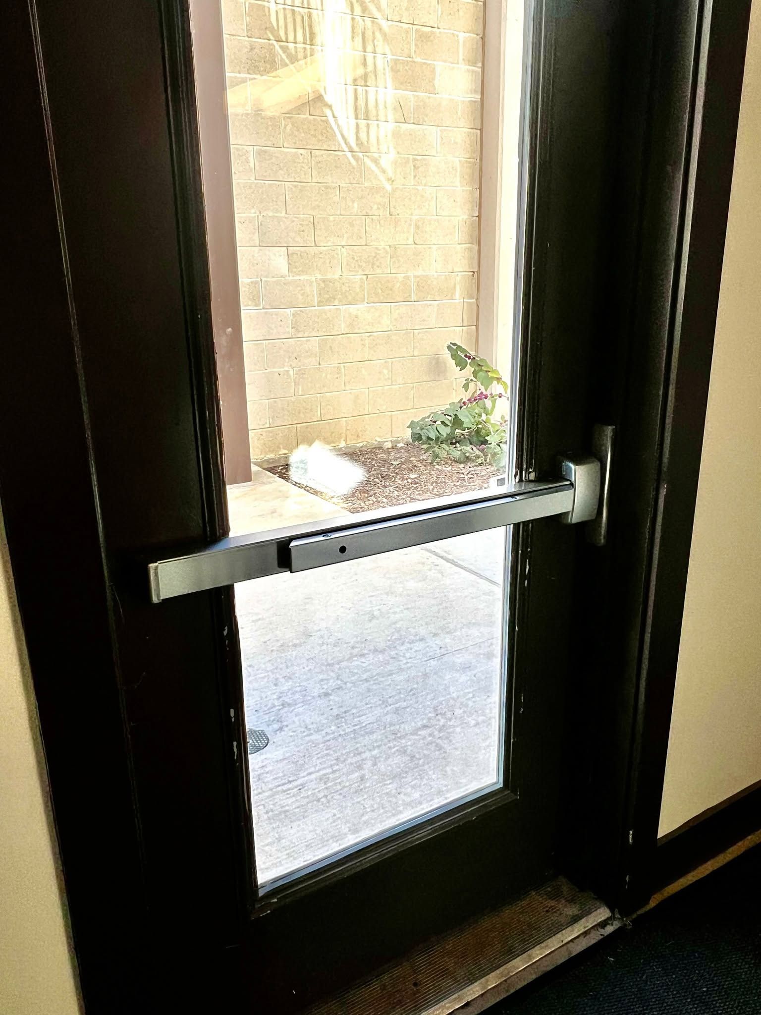 Glass door with a metal push bar, opening to a brick courtyard outside.