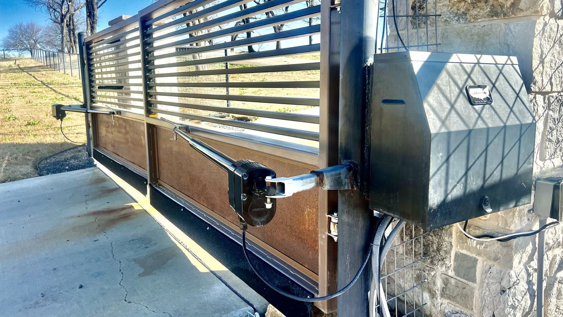Black metal sliding gate with horizontal slats beside a stone pillar and gray utility box outdoors
