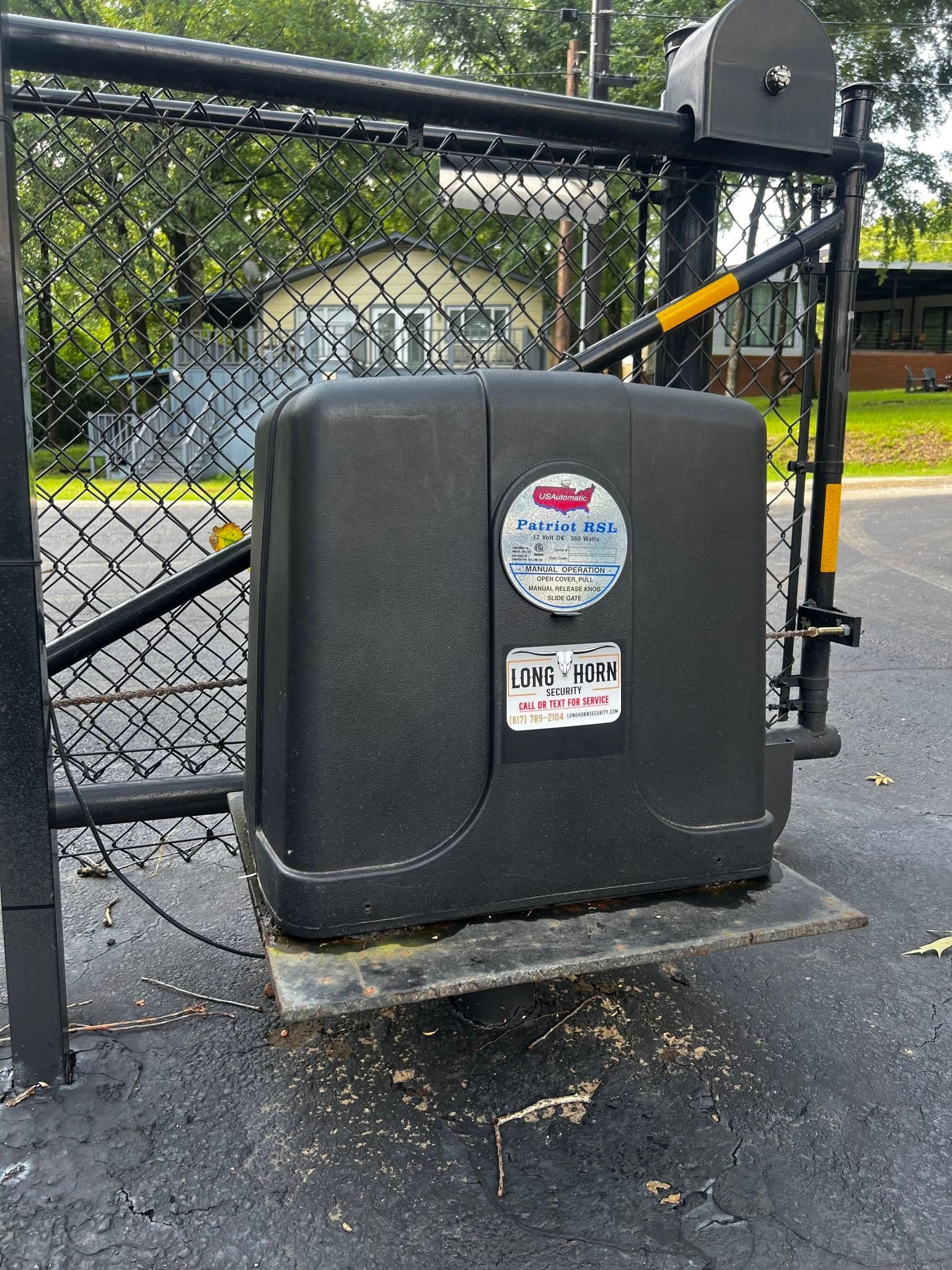 Black utility box beside a chain-link fence and gate in a damp outdoor area