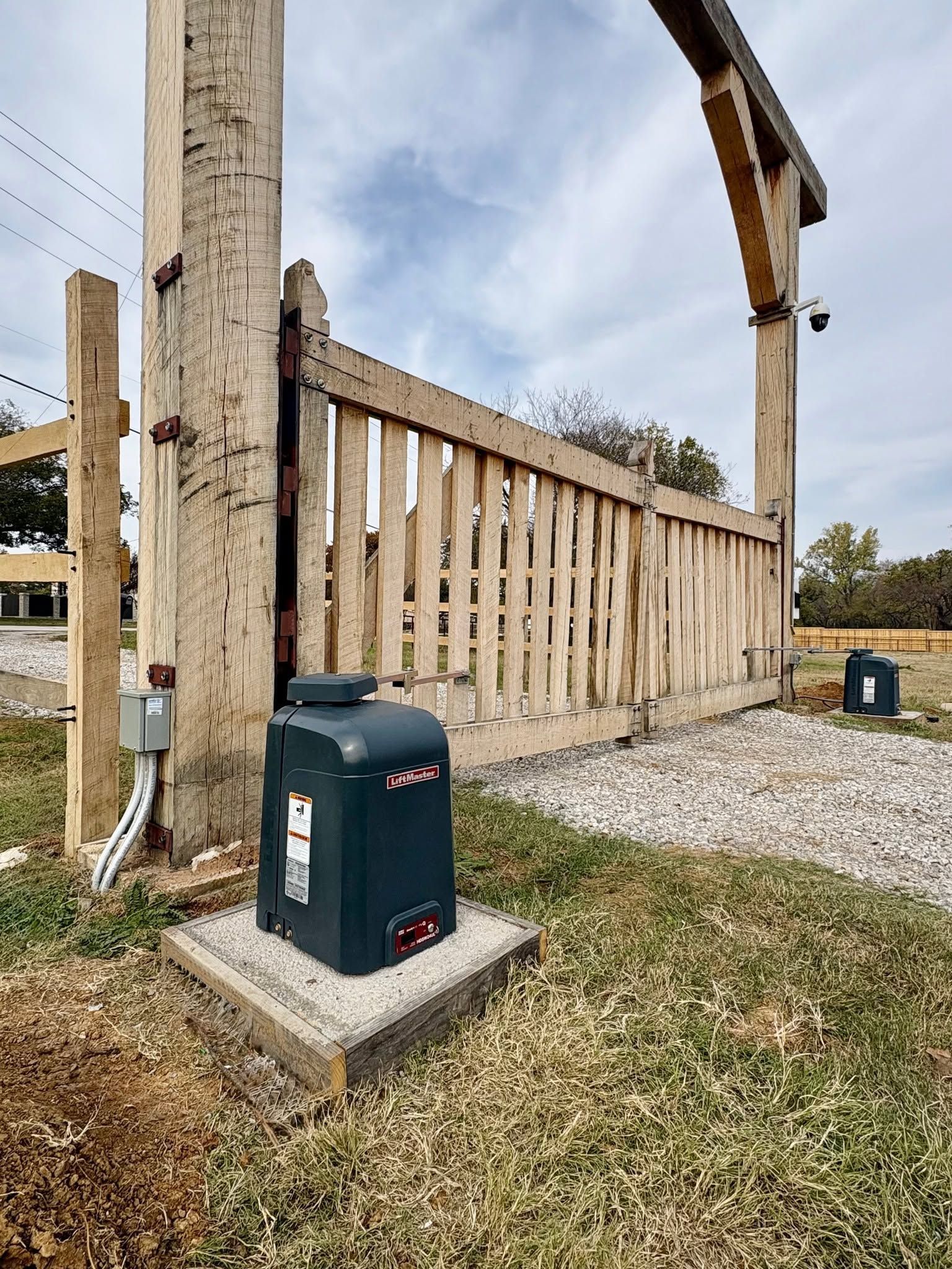 Wooden fence and gate beside a gravel yard, with a green utility box in the foreground.
