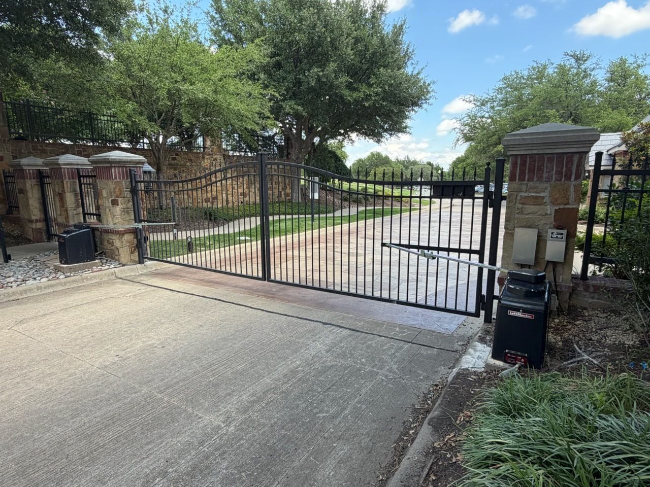 Wooden and black metal driveway gate beside a paved road, with trees in the background.