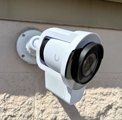 Hands installing a white security camera on a beige wall, holding a red tool nearby.