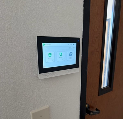 Gloved hands enter a lit keypad door lock outside a house at night, with a red sensor light above.