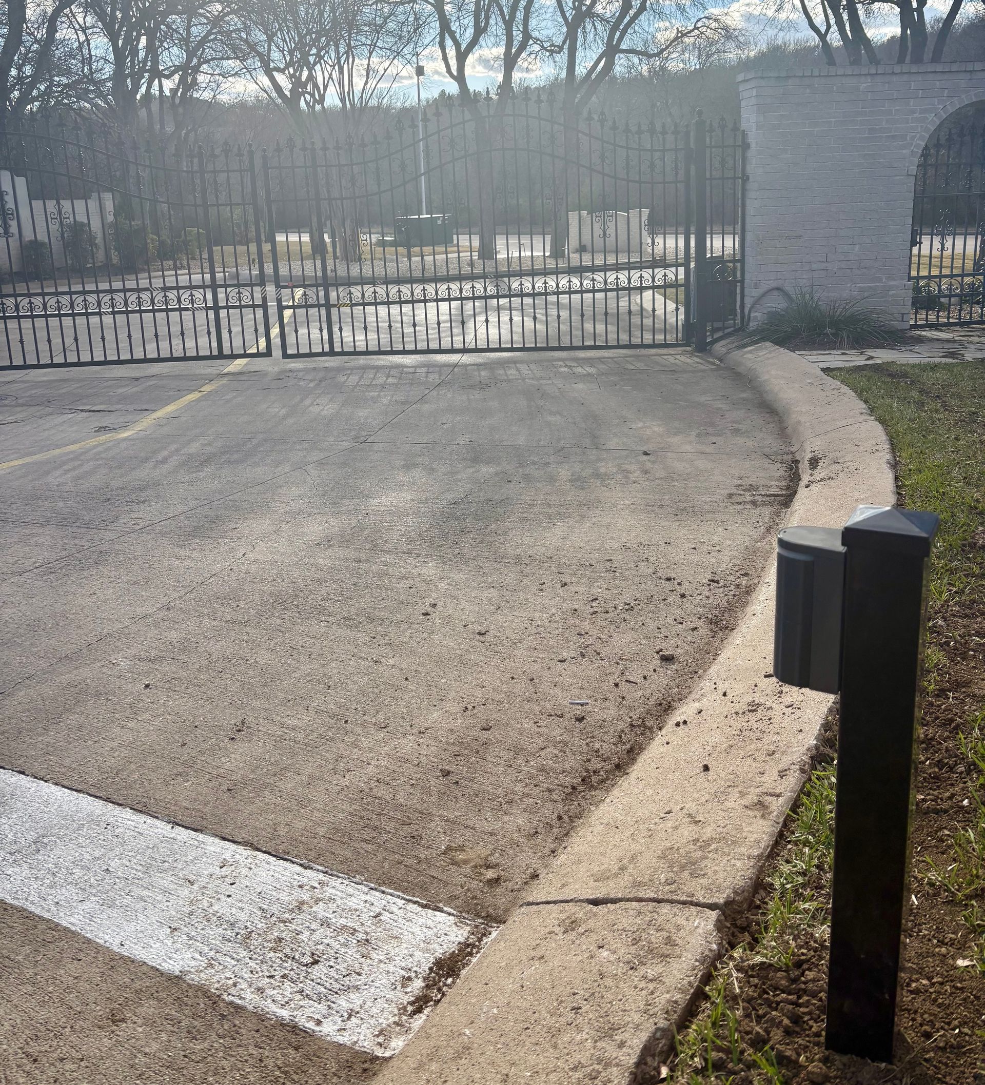 Closed black gate blocking a driveway at a park entrance, with concrete curb and trees in the background