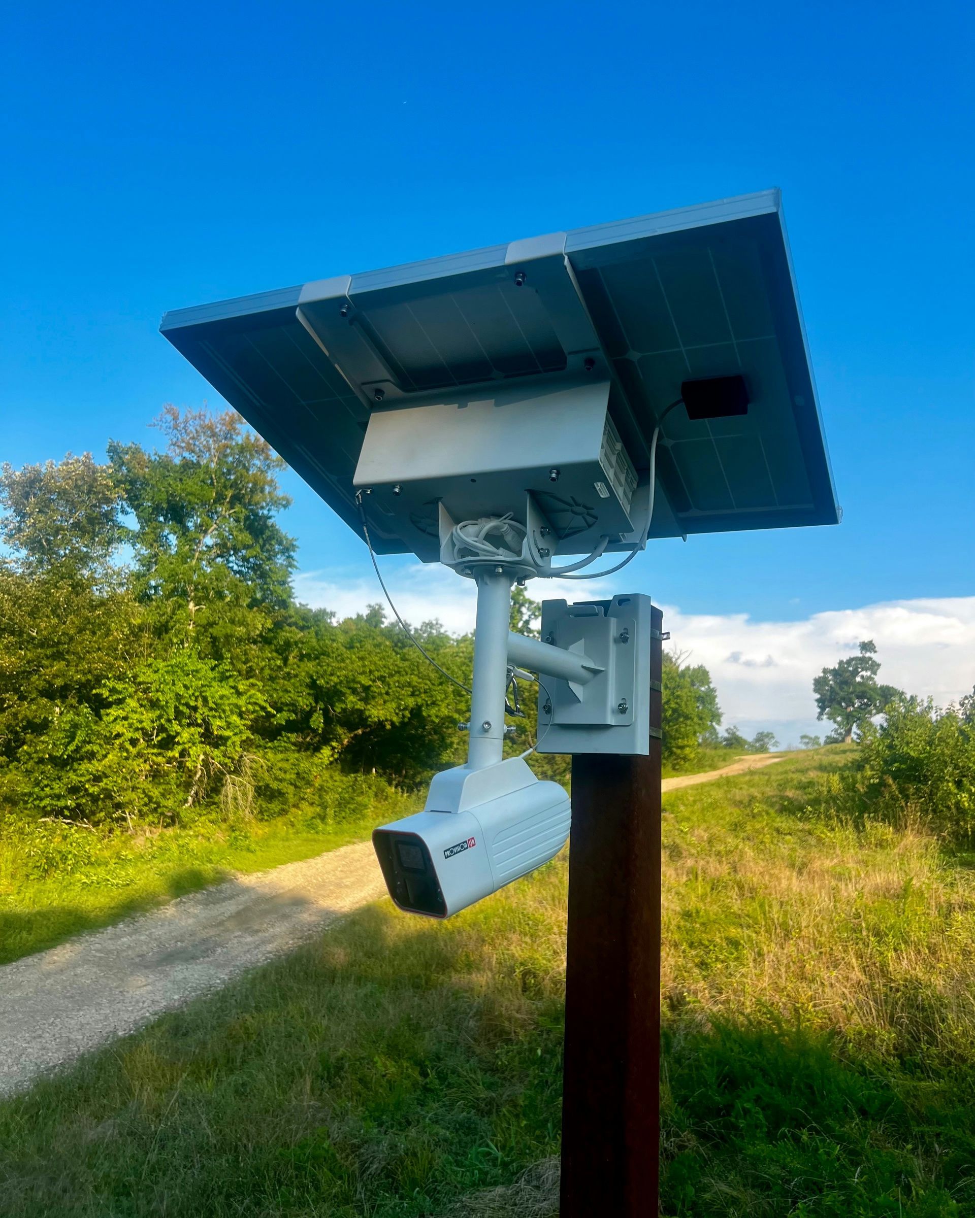 Solar-powered security camera mounted on a post beside a grassy path under a blue sky