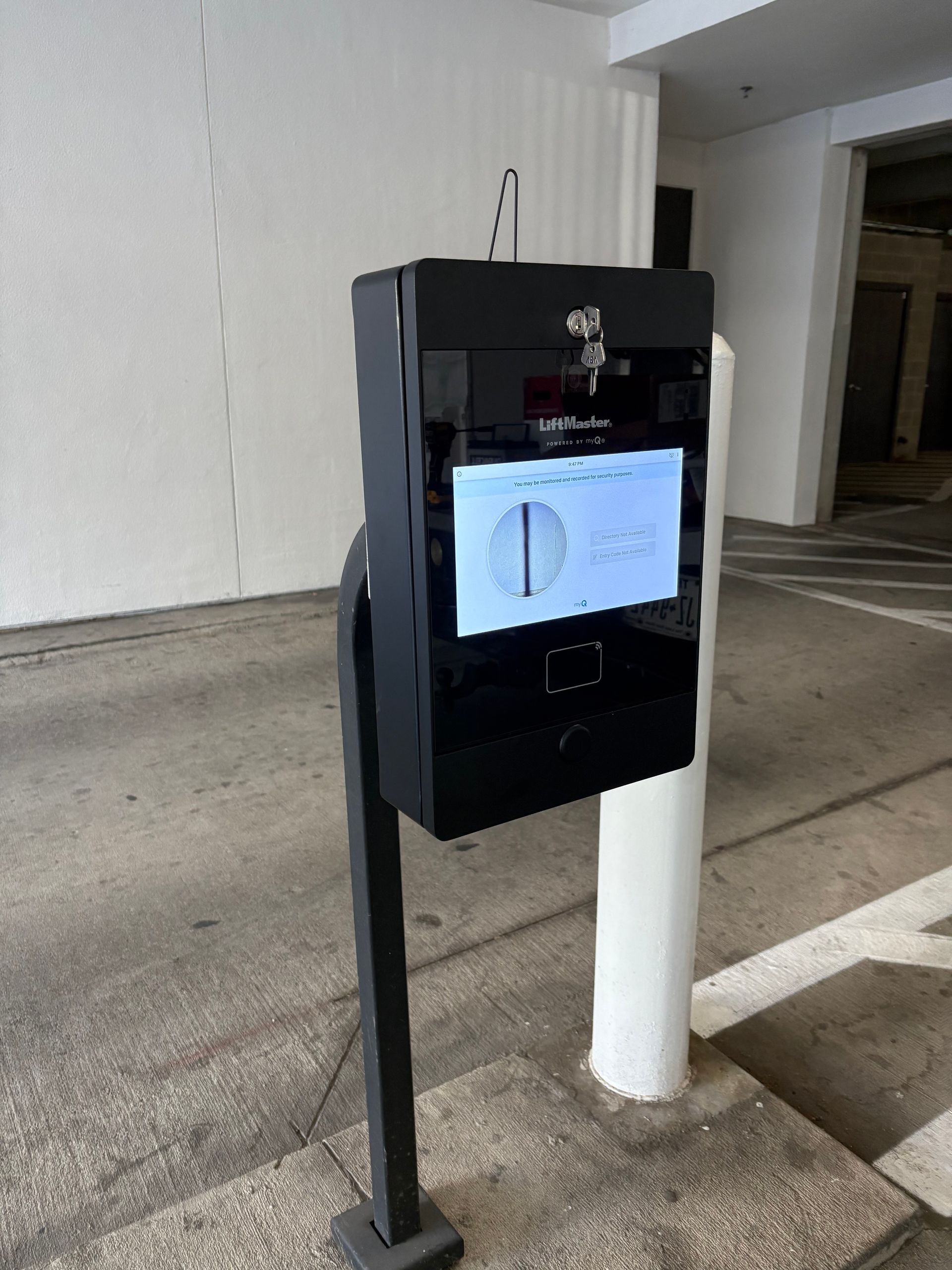Black kiosk mounted on a post beside a white pillar in a parking garage