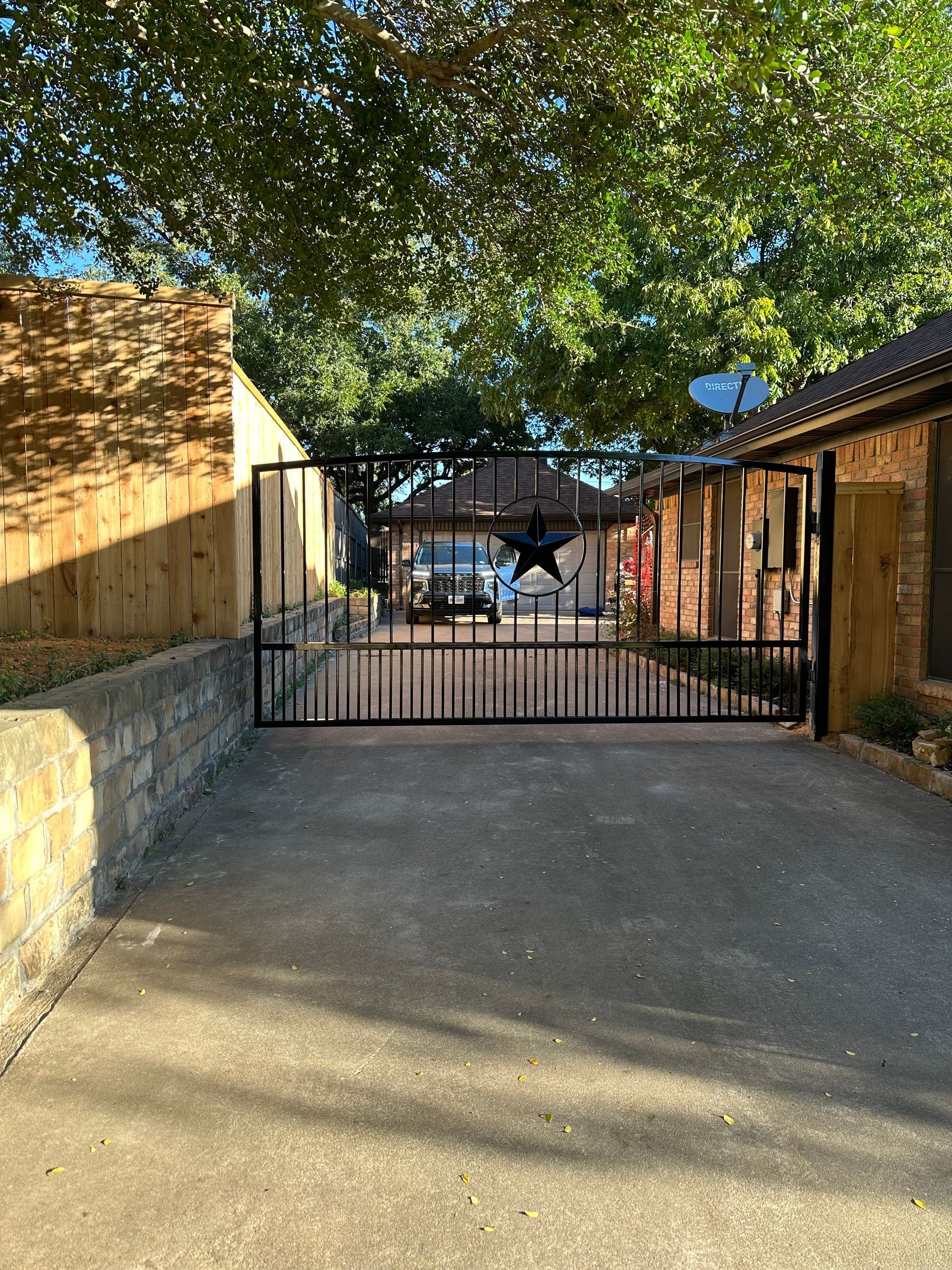 Gated driveway between wooden buildings under a tree, with a parked car visible beyond the gate.