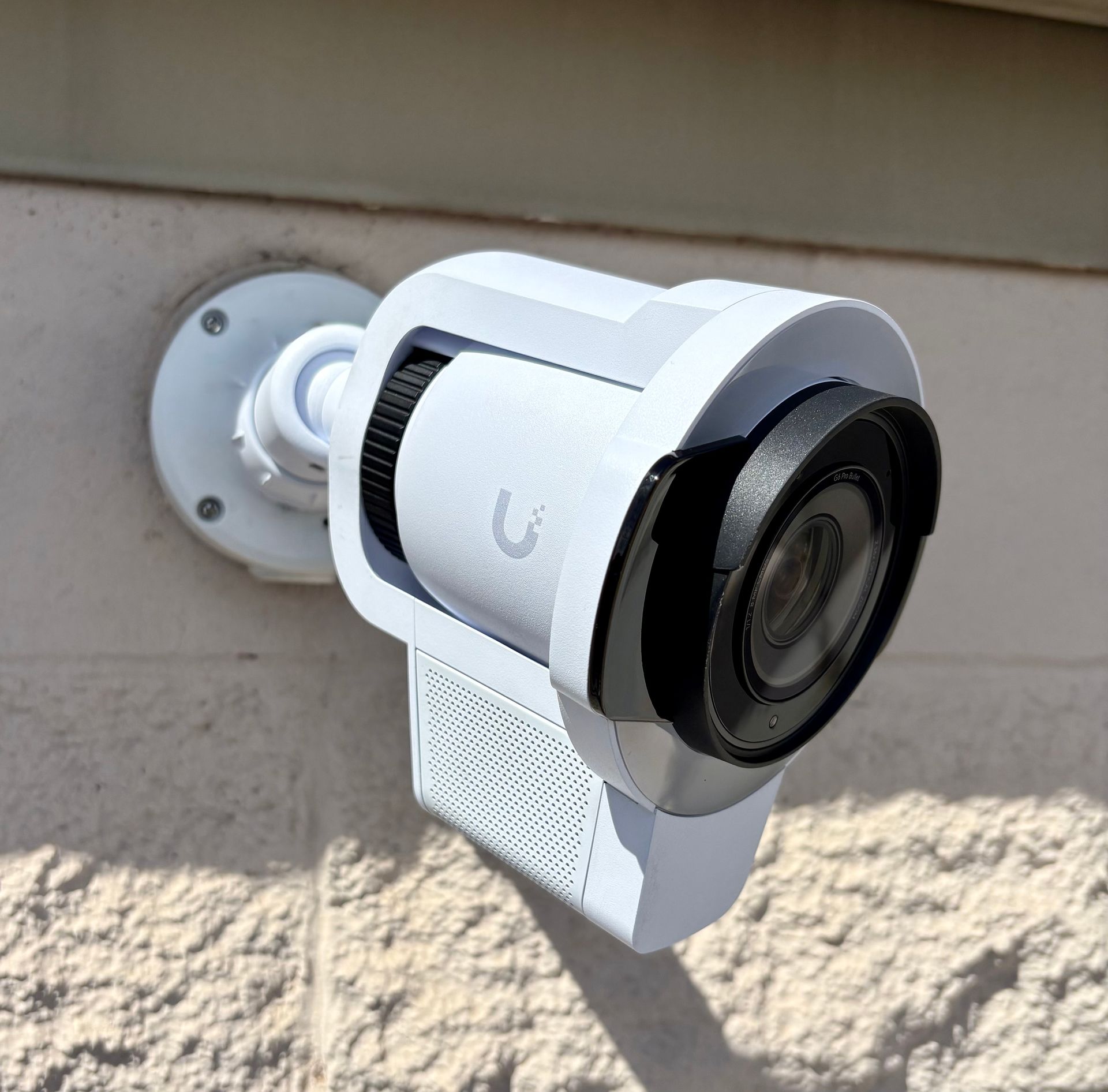 White security camera mounted on a beige exterior wall, facing outward