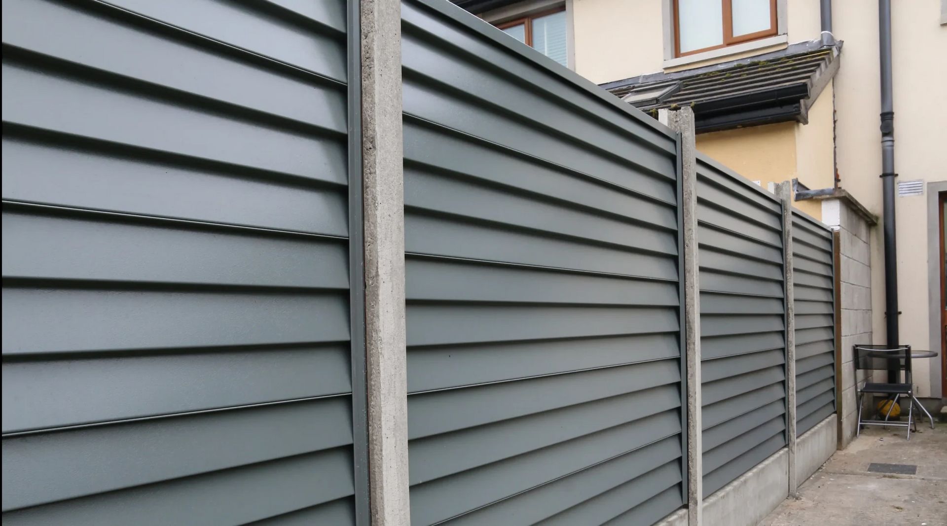 Gray metal slat fence along a narrow alley beside a beige house