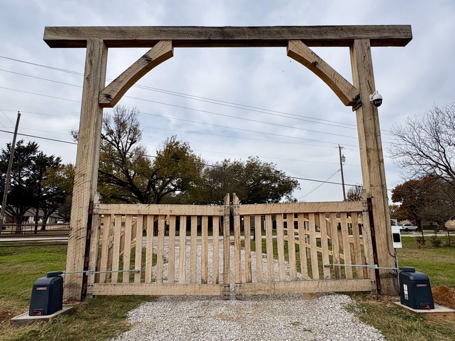 Rustic wooden gate with white slats and overhead beam in a park-like outdoor setting