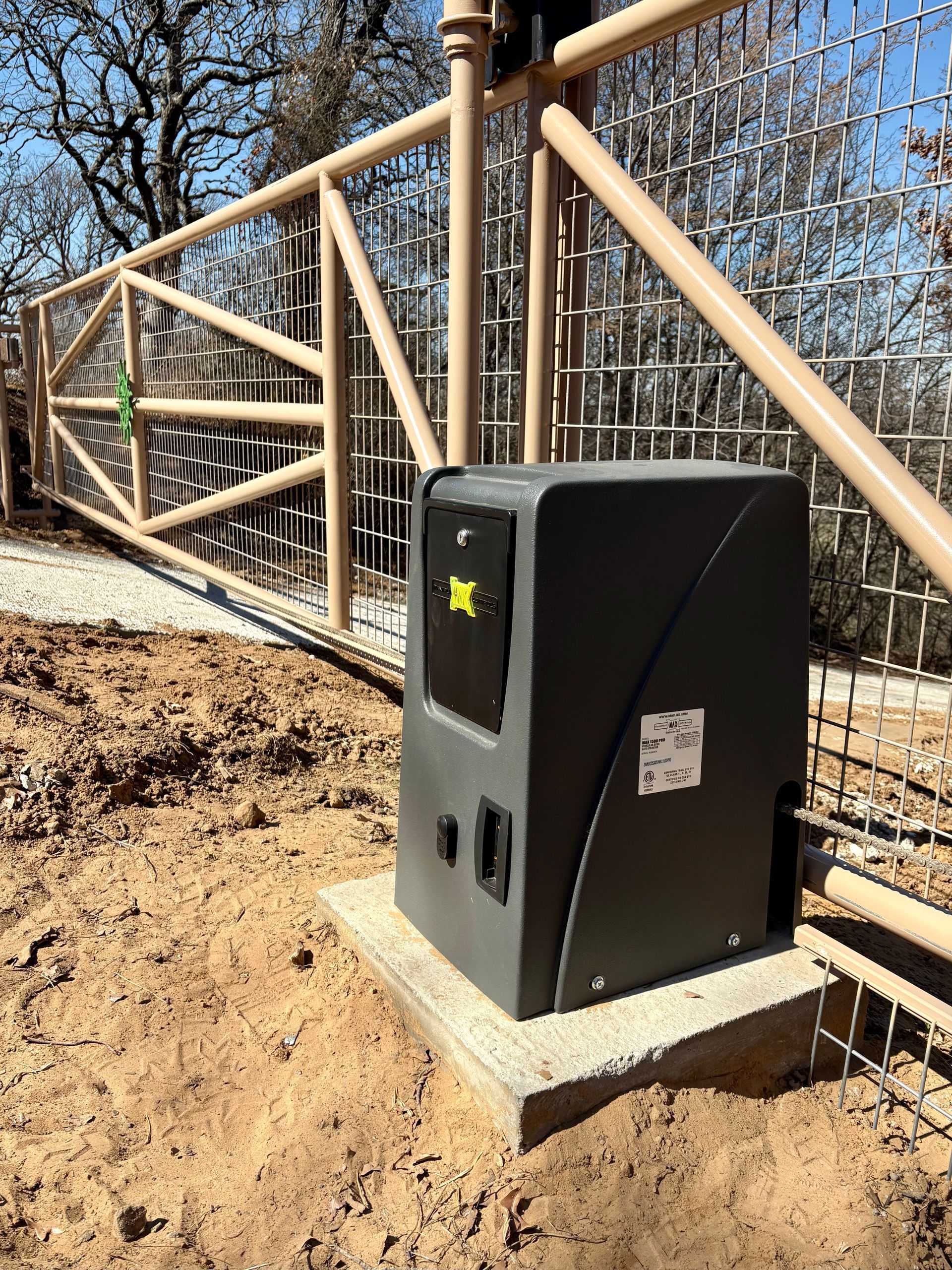 Black gate motor beside a tan metal fence on a dirt slope, outdoors in a wooded area