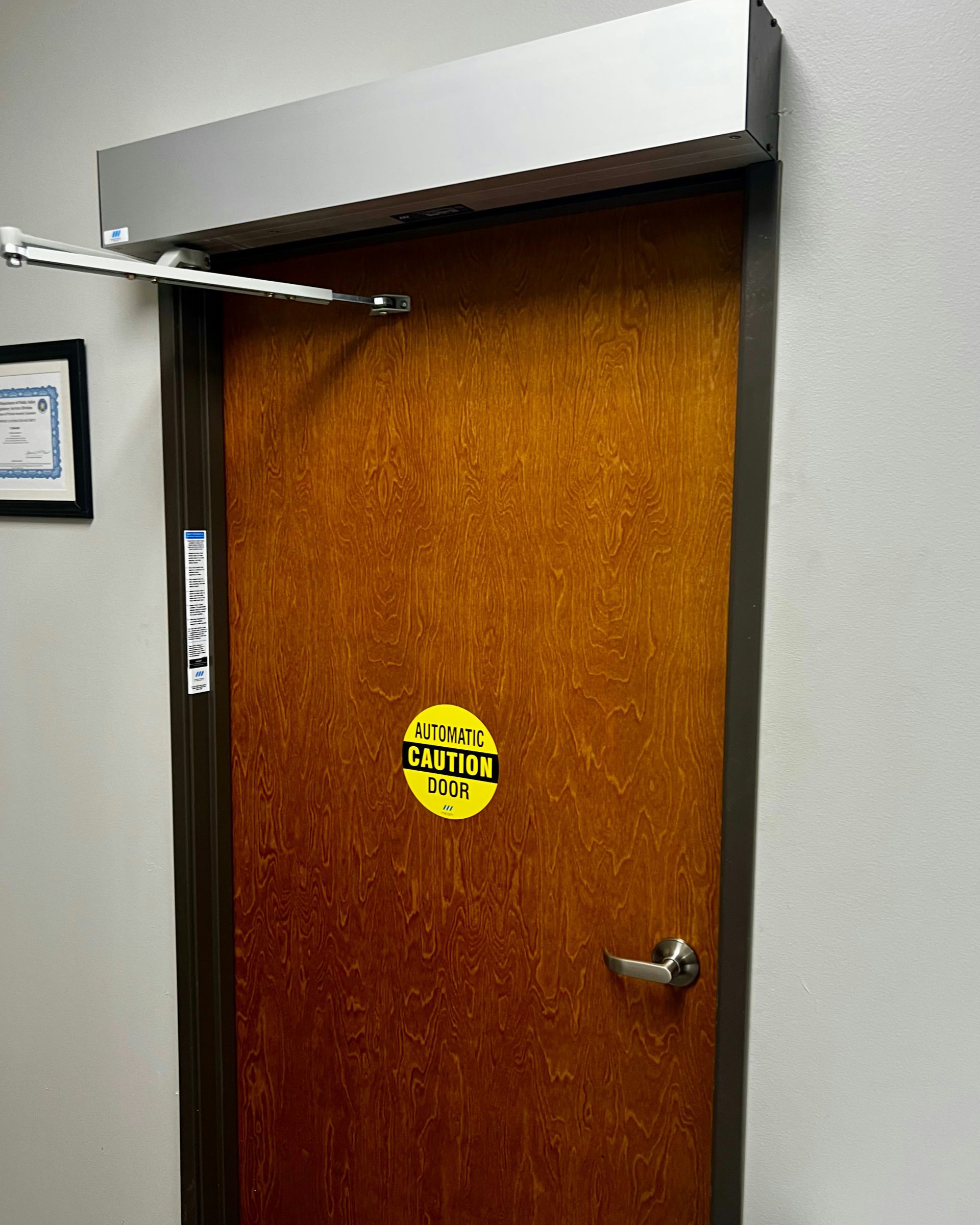 Closed wooden office door with a silver handle, yellow notice, and overhead door closer.