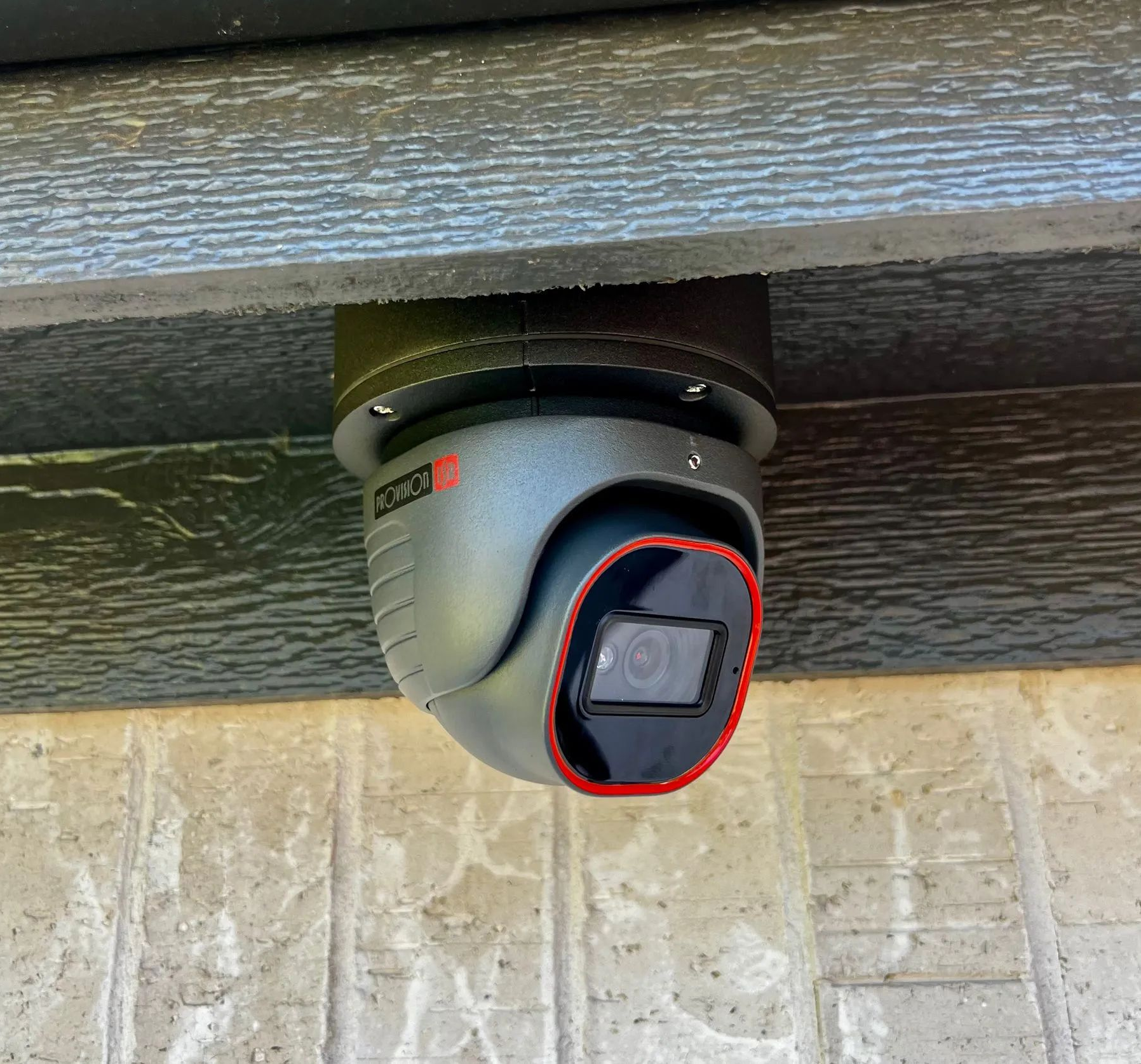 Black security camera mounted under an eave, with the lens circled in red.