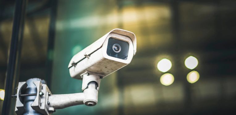 Security camera mounted on a pole, angled upward with blurred city lights in the background