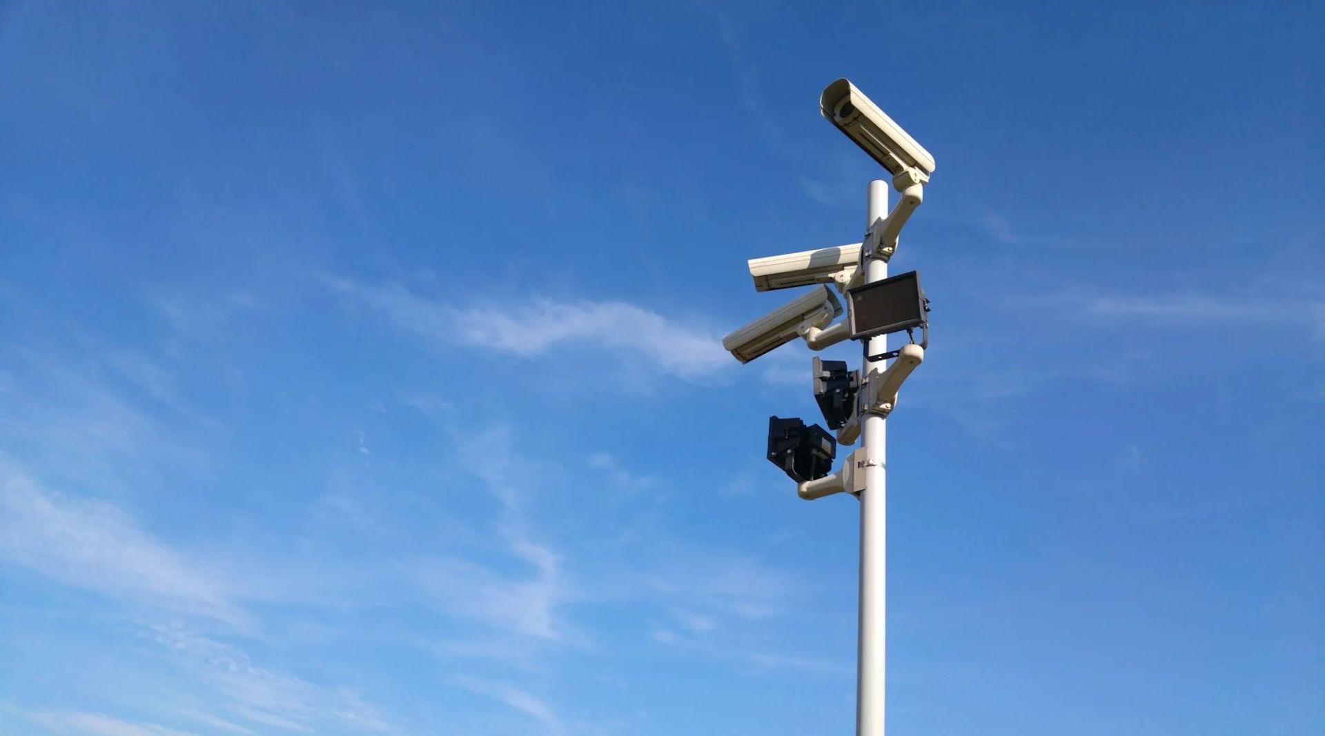 Tall light pole with several mounted floodlights against a blue sky