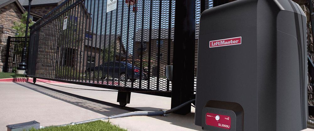 Black metal gate and fence beside a driveway, with a large gray security device in the foreground.