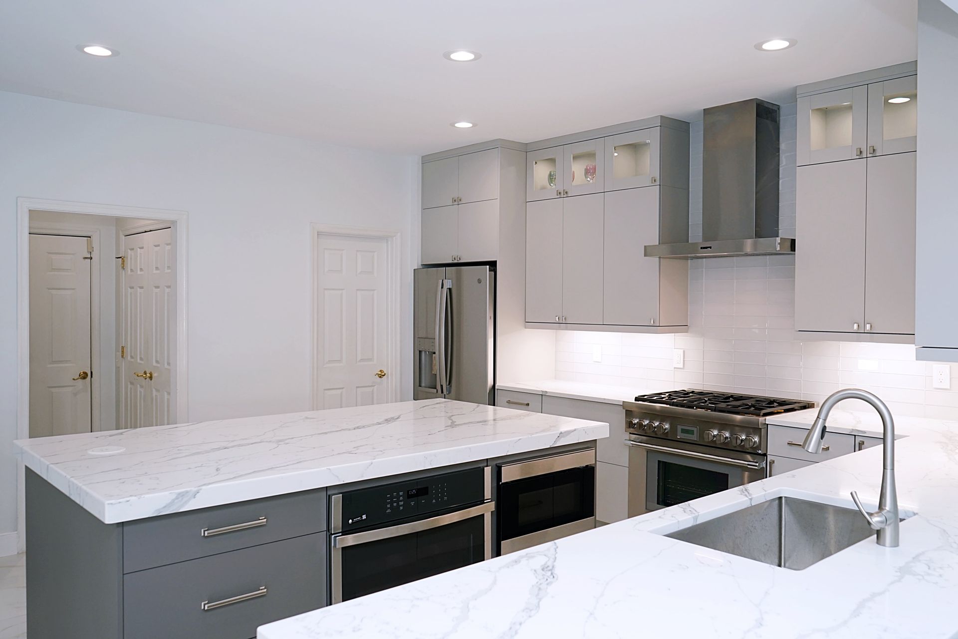 Modern white kitchen with marble island, stainless appliances, and gray cabinets