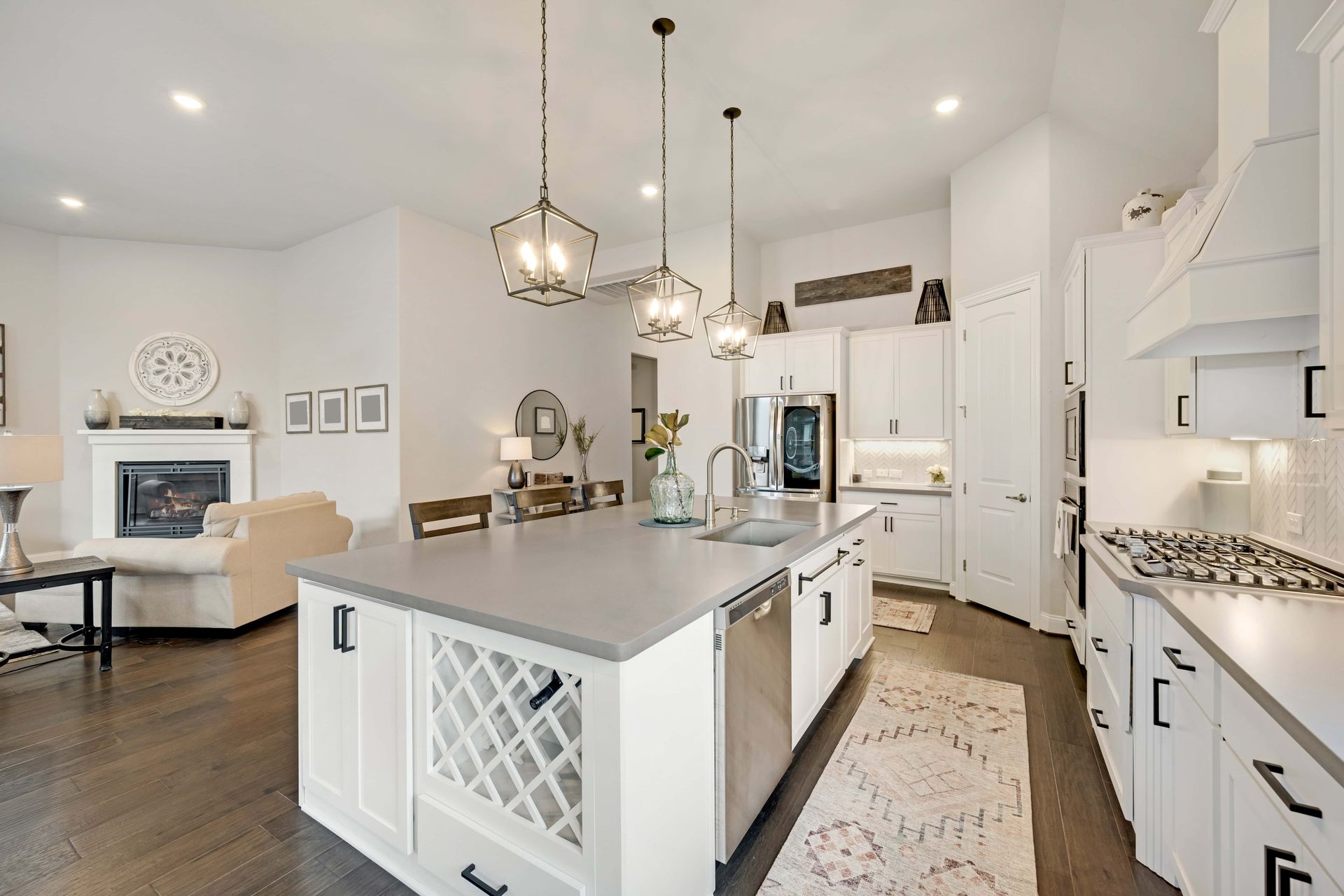 Bright white kitchen with island, pendant lights, and adjacent living room with fireplace
